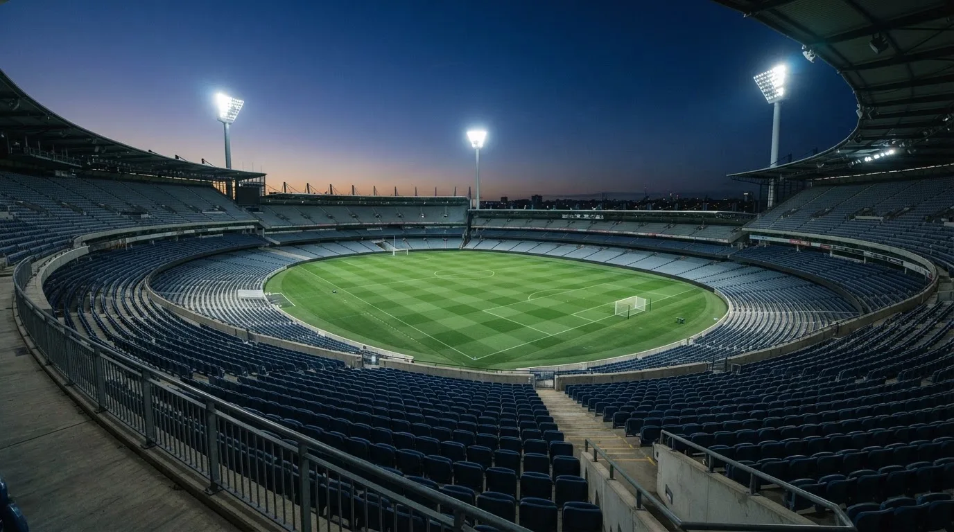 An empty football stadium with floodlight masts at dusk