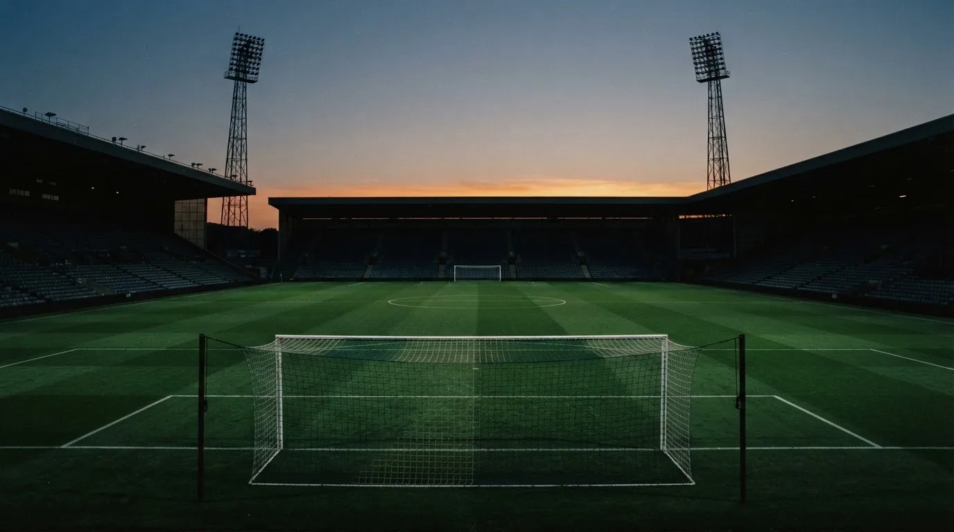 An empty football stadium with floodlight masts at dusk